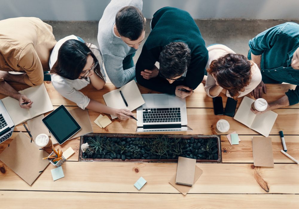 Top view of young modern people in smart casual wear using modern technologies while working in the creative office